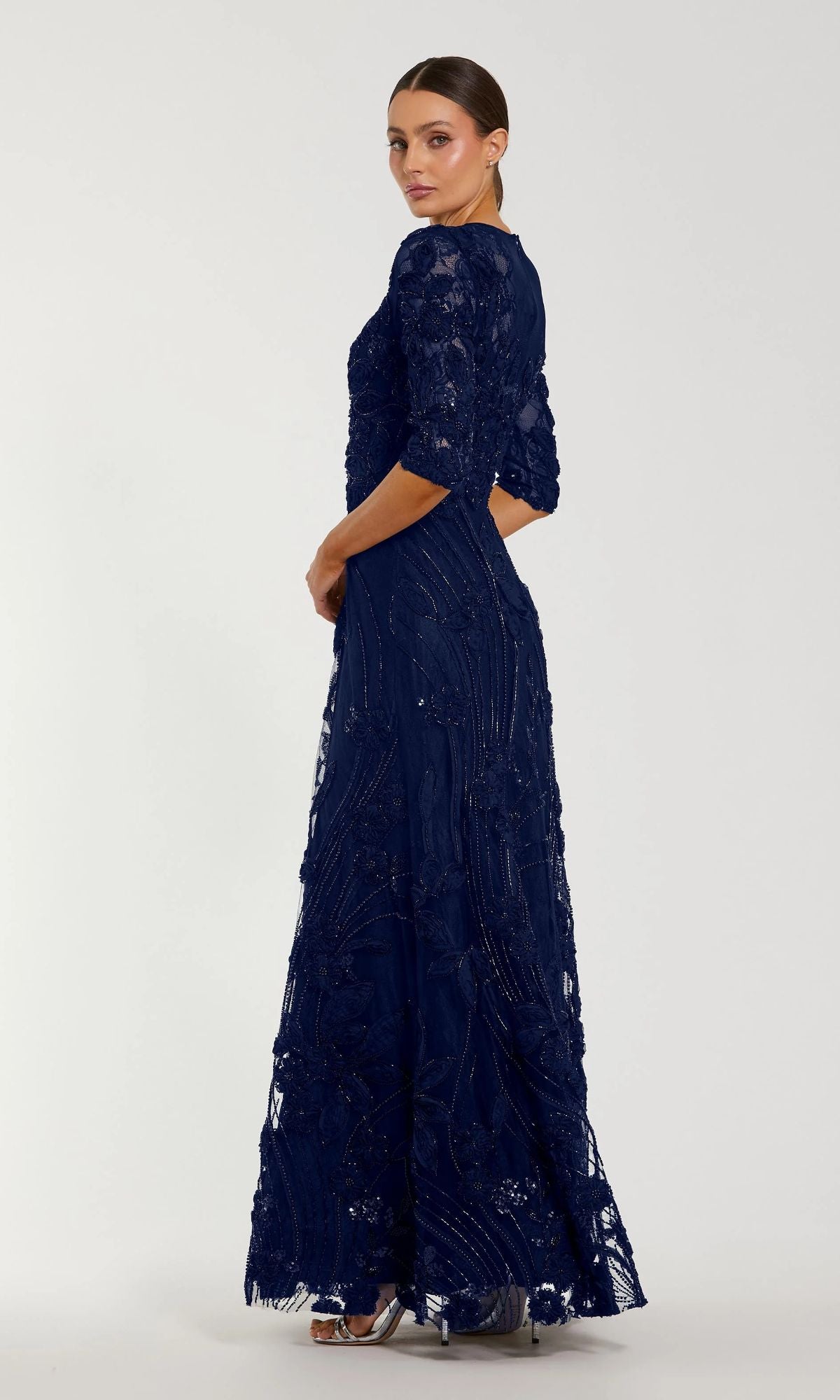 A woman in profile poses against a plain light background, wearing the Mac Duggal 69016 Long Sleeve Beaded Formal Gown—a sophisticated floor-length navy option for the mother of the bride.
